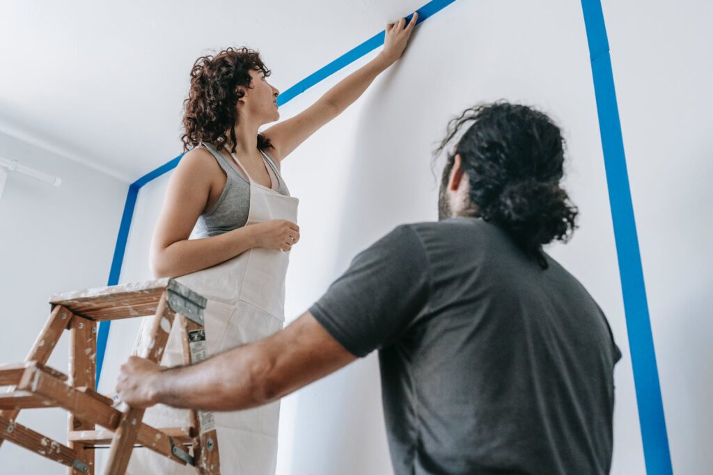 man standing beside woman on a stepladder painting the wall