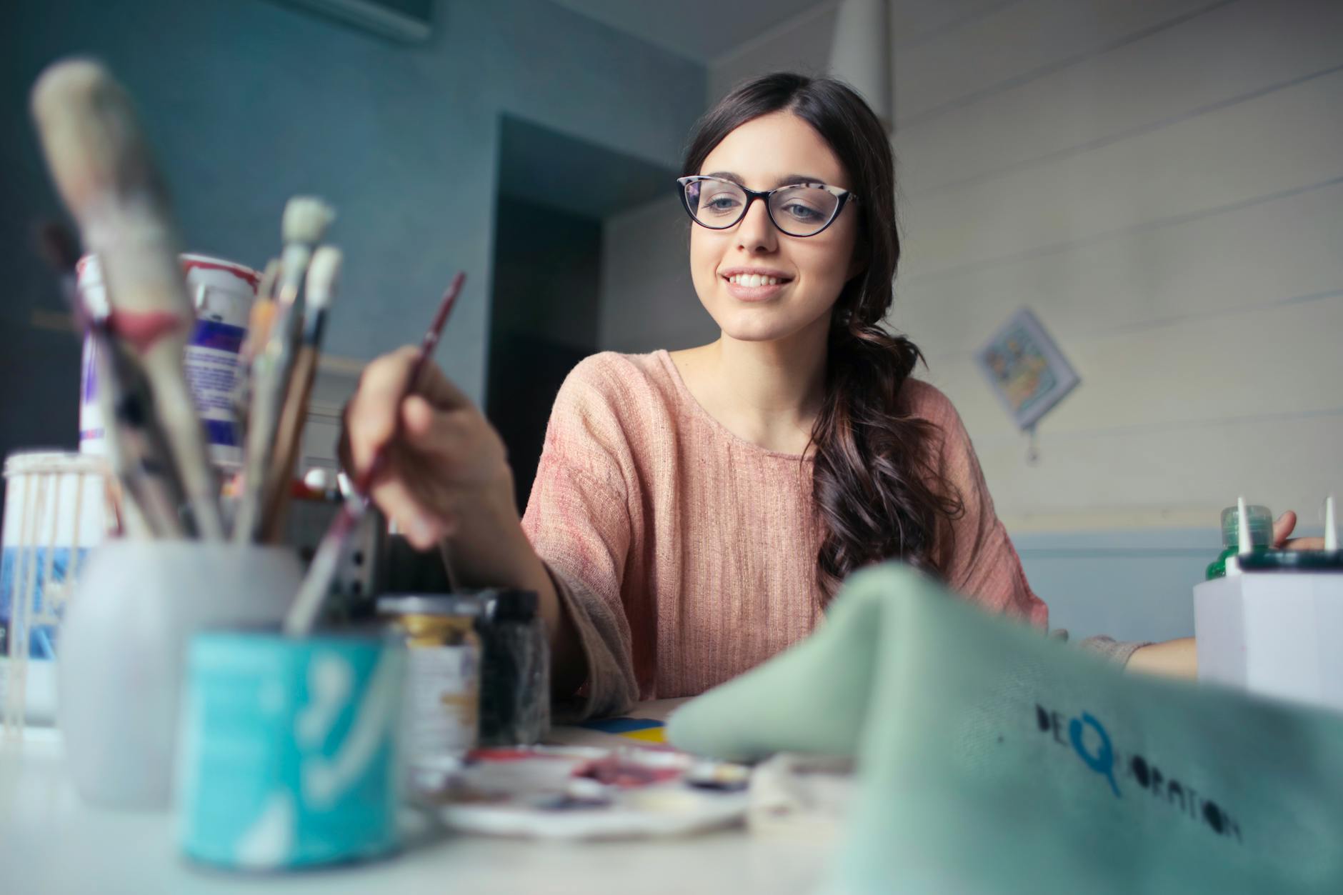 woman in brown long sleeved shirt wearing eyeglasses holding paint brush