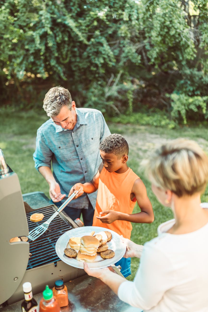 boy flipping hamburgers at a barbecue with his adoptive parents